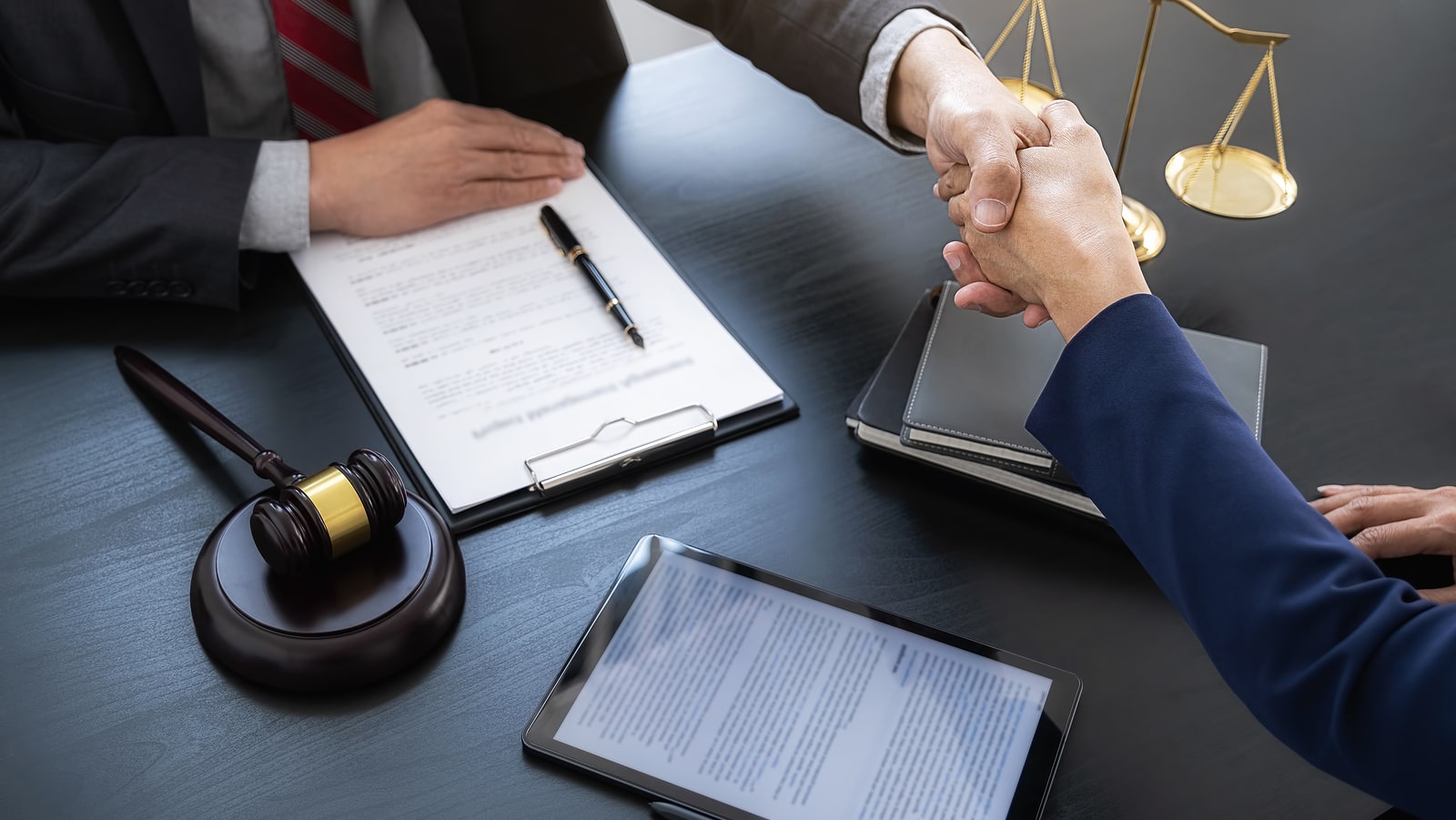 Image of a probate attorney shaking hands with a client over some documents and contracts on a table