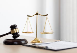 Image of the scales of justice, a gavel, and a document on a clipboard on a desk