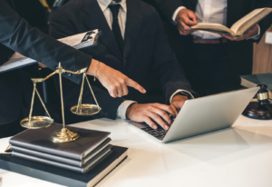 Image of attorneys consulting over a laptop on a desk with the scales of justice on a pile of books