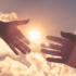 Image of two hands reaching for each other in front of a cloudy sky