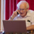 An older man using a laptop and talking on the phone